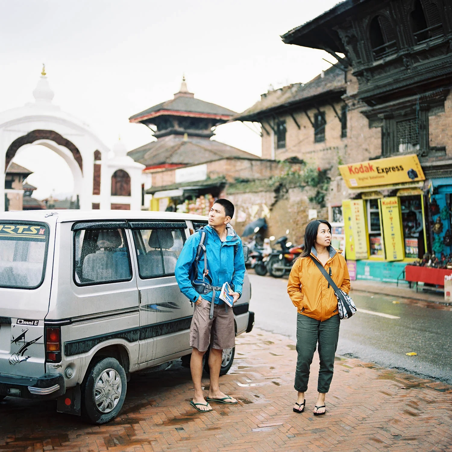 Two travelers standing beside a vehicle in a Nepalese square.