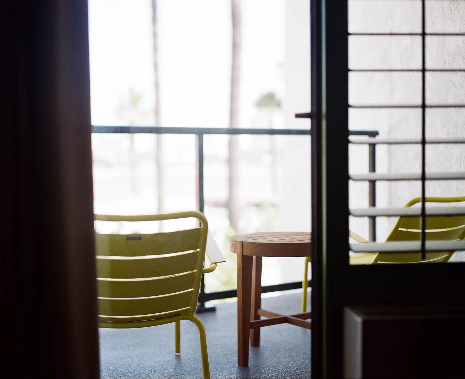 Green chairs and a small table on a bright balcony beyond a doorway.