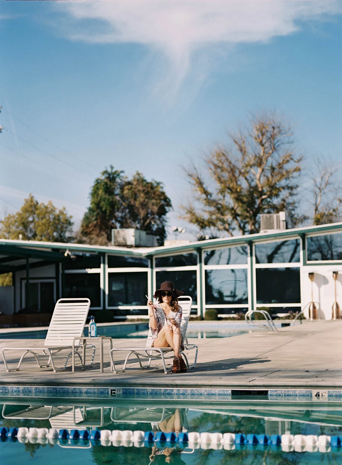 Woman sitting beside a pool in front of a modern building.