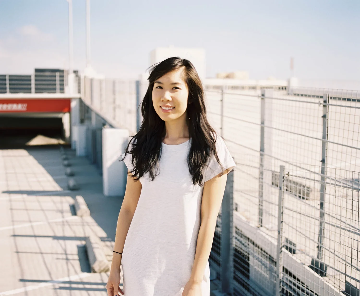 Smiling woman in a pale dress beside a rooftop fence.