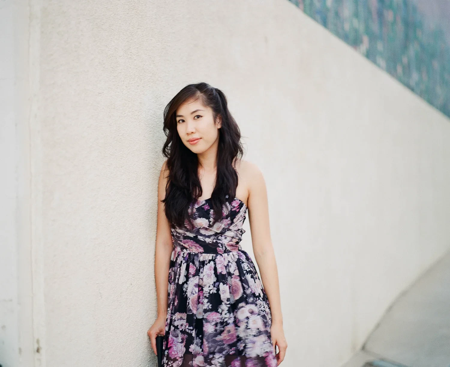 Woman in a floral dress standing beside a pale wall.