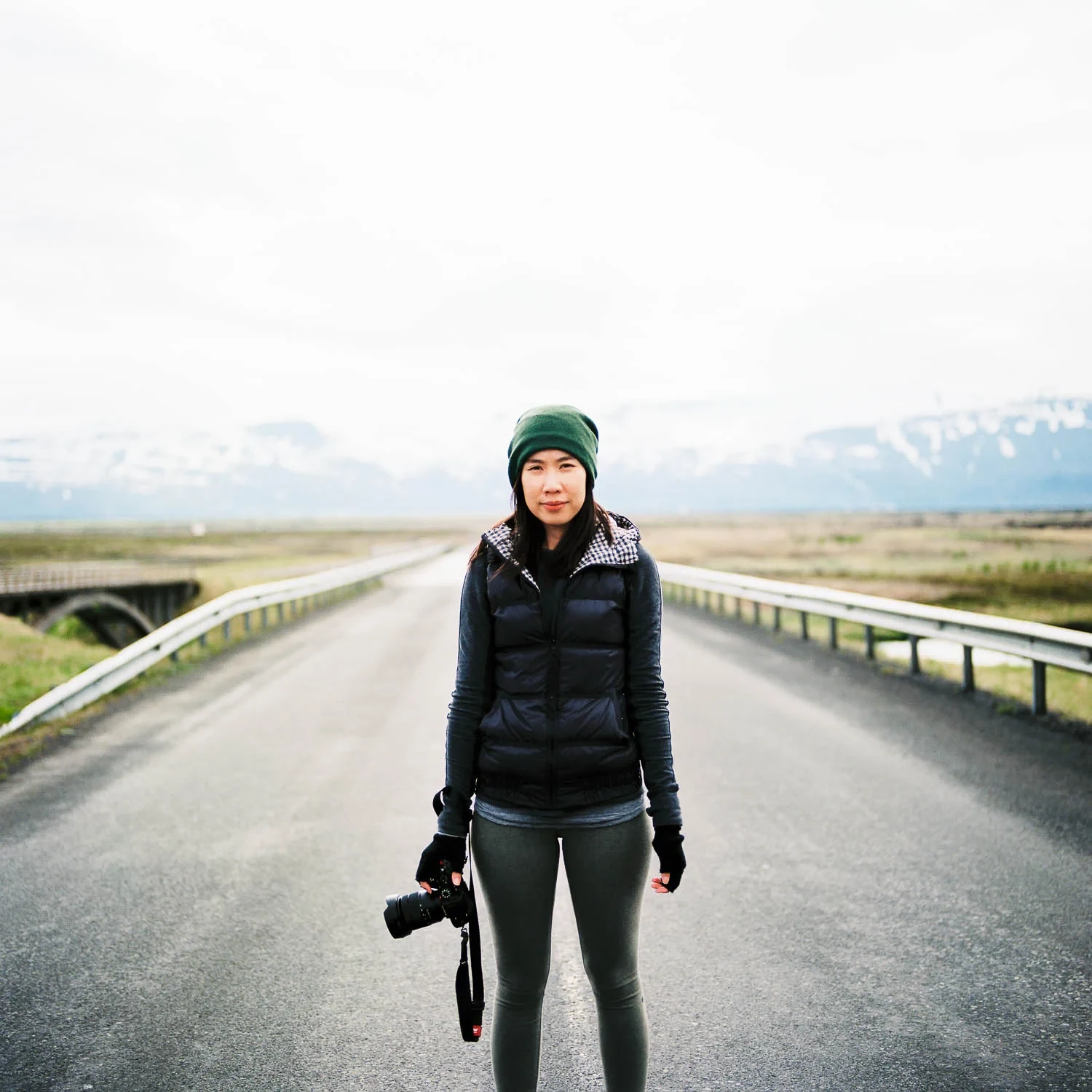 Traveler with a camera standing on a straight road toward distant mountains.