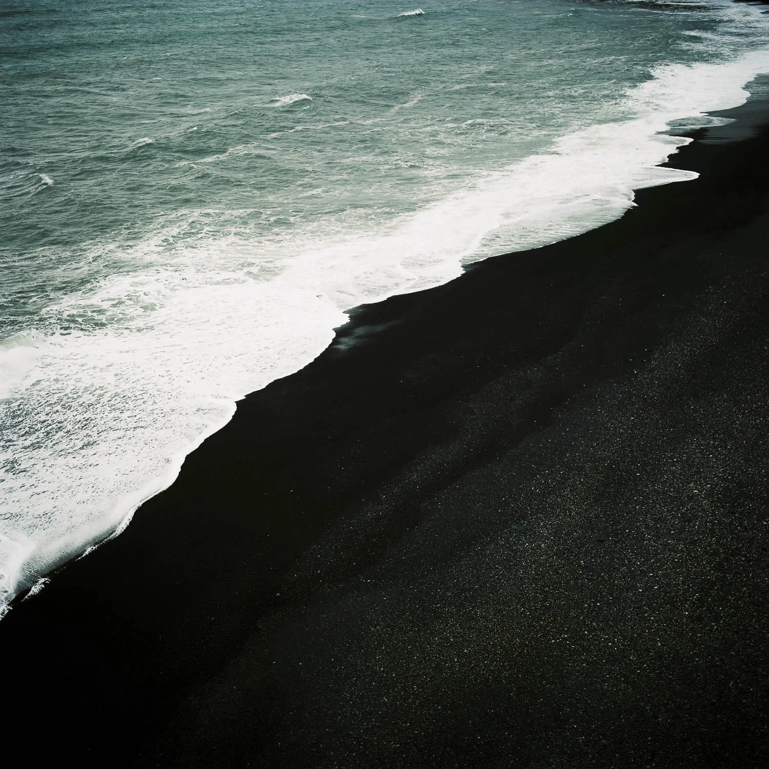 White ocean surf washing over a black-sand beach.