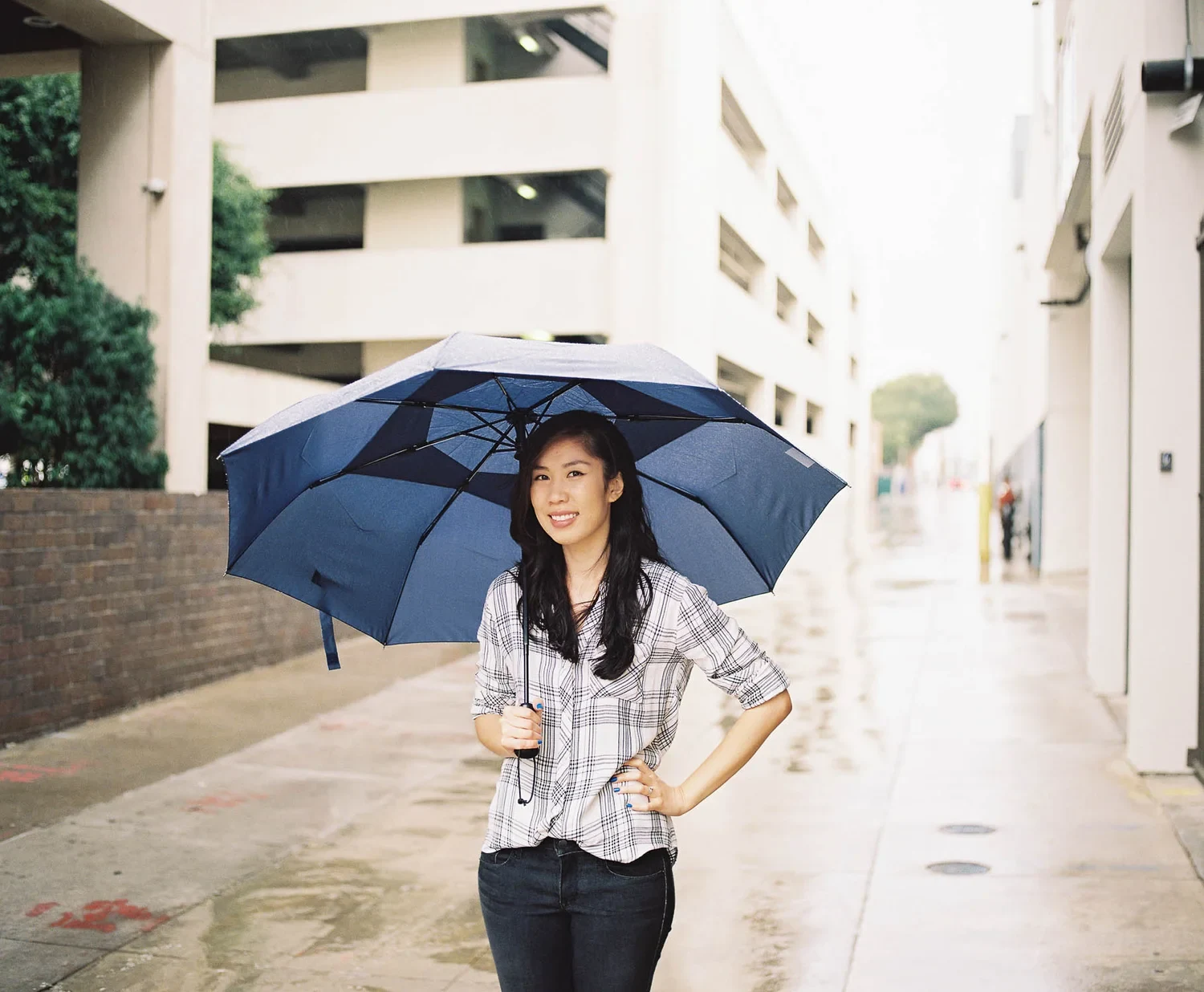 Woman holding a dark umbrella on a bright city street.