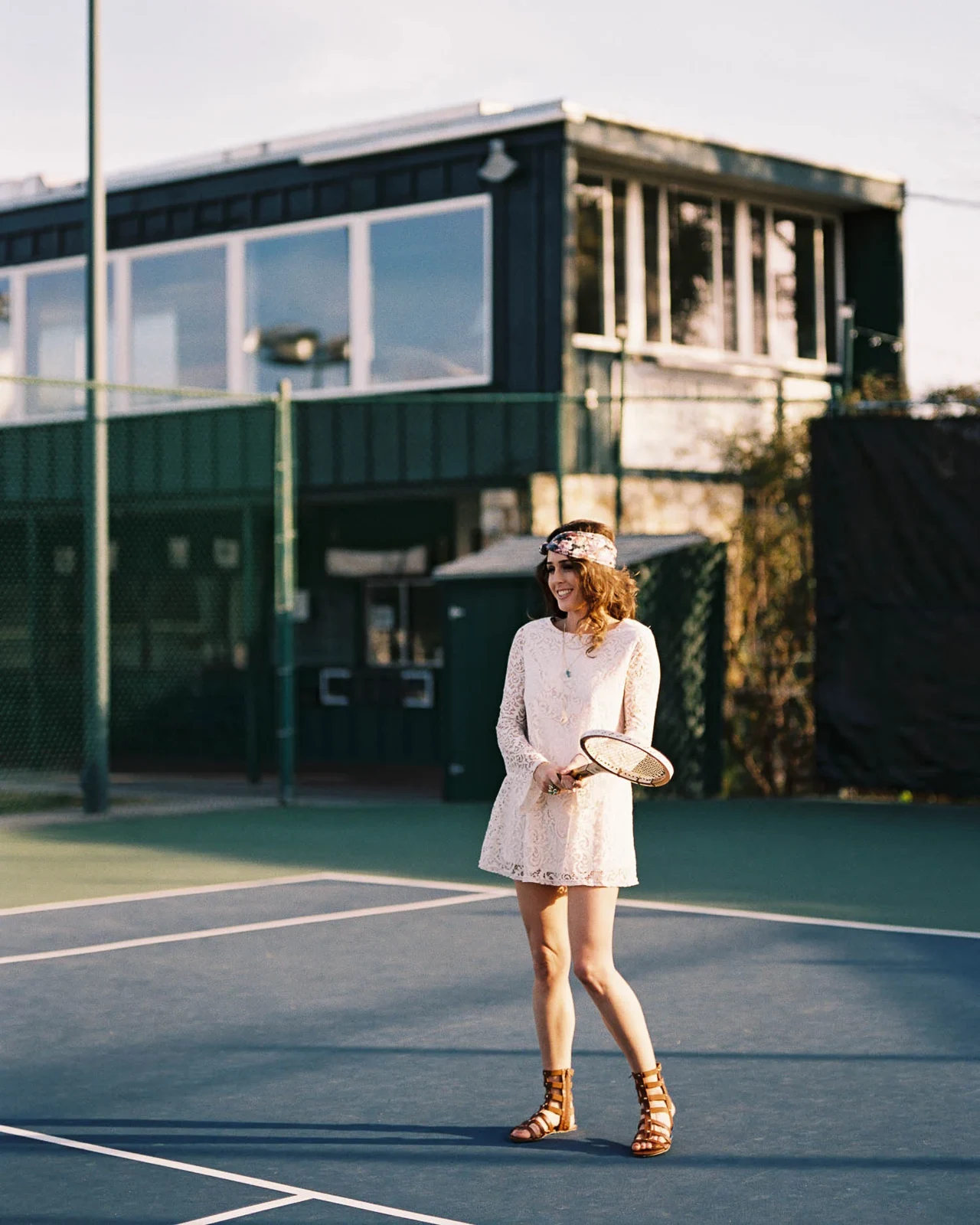 Woman in a pale outfit and hat standing on an outdoor court.