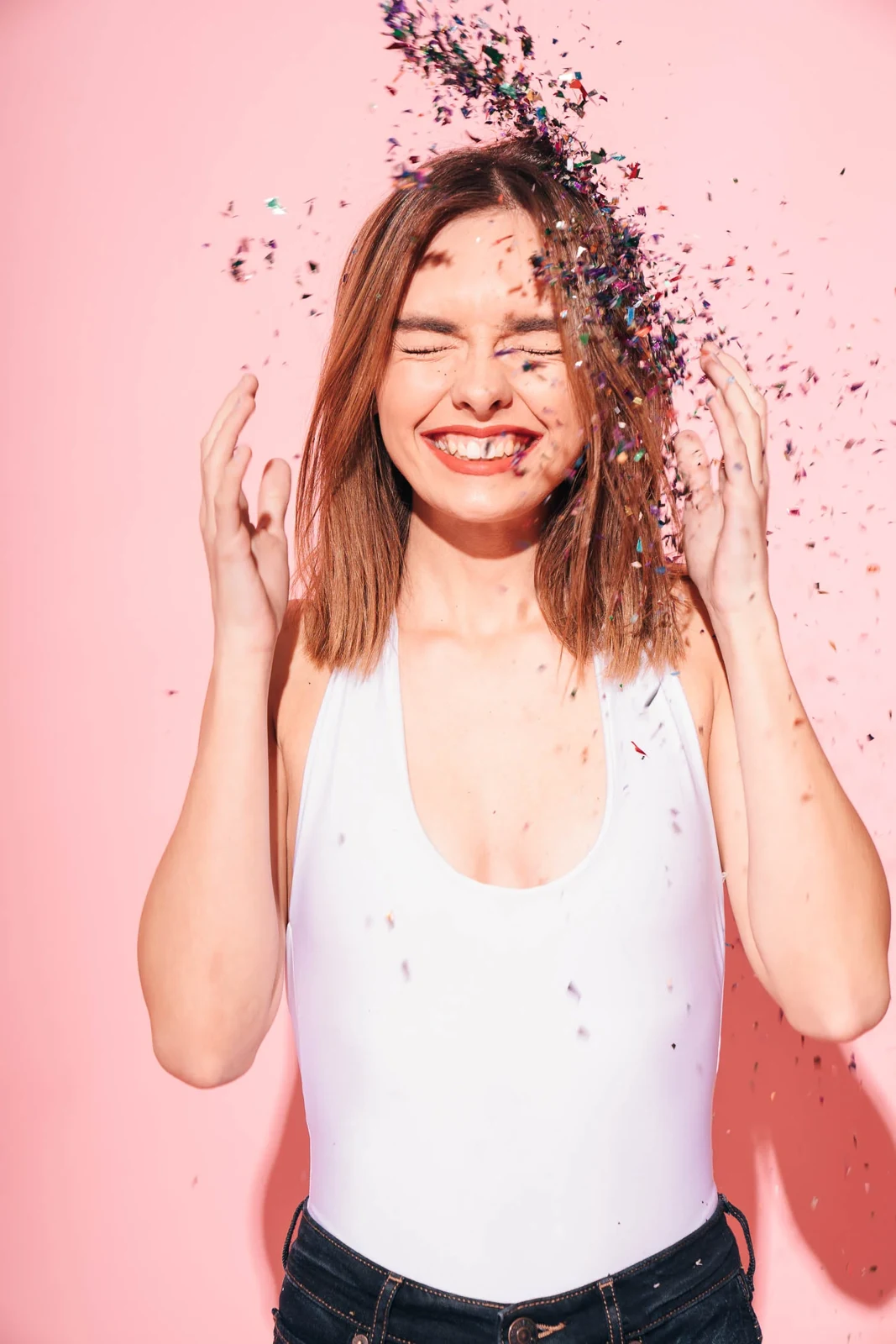 Woman smiling as confetti falls against a pink background.