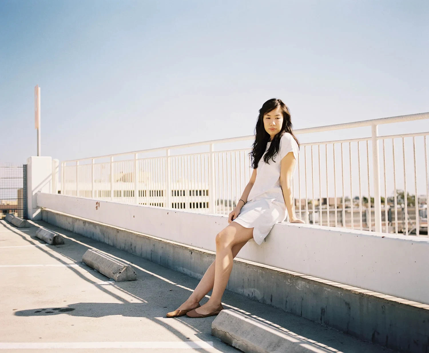 Woman sitting on a low rooftop wall in sunlight.