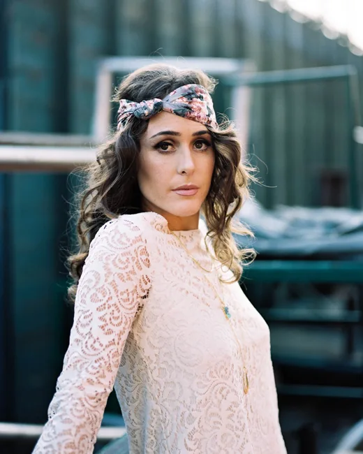 Woman in a white lace top with a patterned headband outdoors.