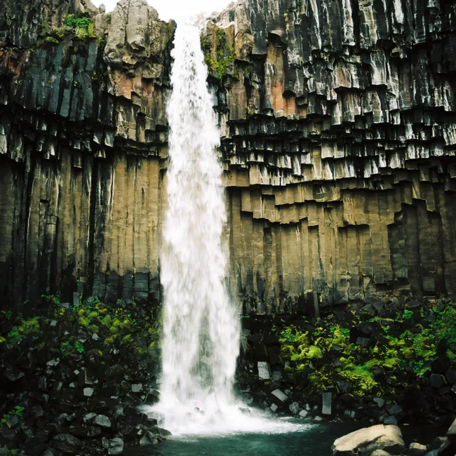 Tall waterfall descending between dark basalt columns.