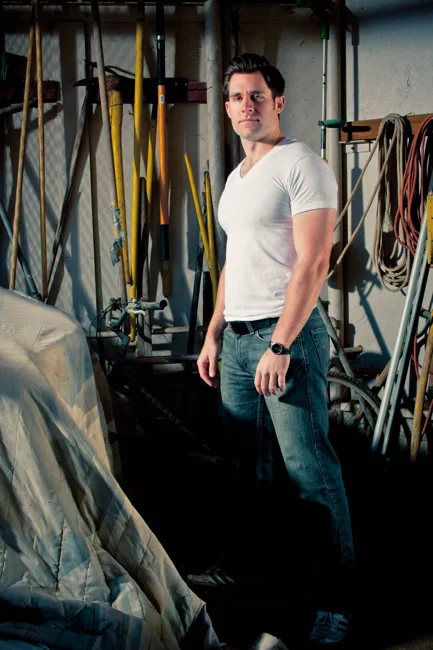 Man in a white T-shirt standing among tools in a workshop.
