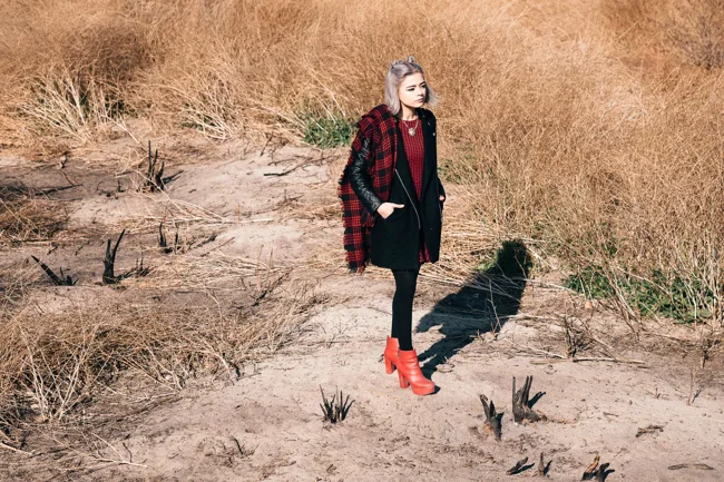 Model in red boots standing on a sunlit path through dry grass.