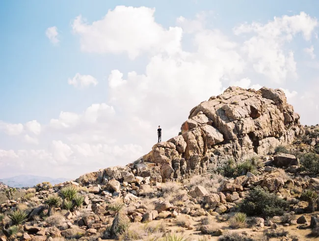 Rocky desert ridge beneath a bright sky with scattered clouds.