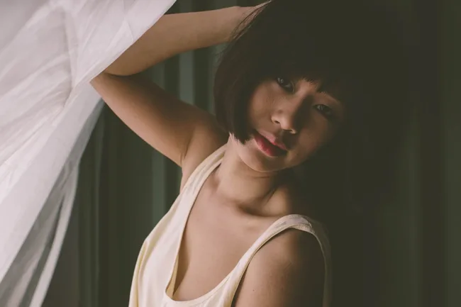 Woman lifting a sheer curtain in a softly lit room.