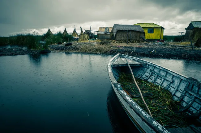 Small boat on still water beside lakeside homes beneath dark clouds.