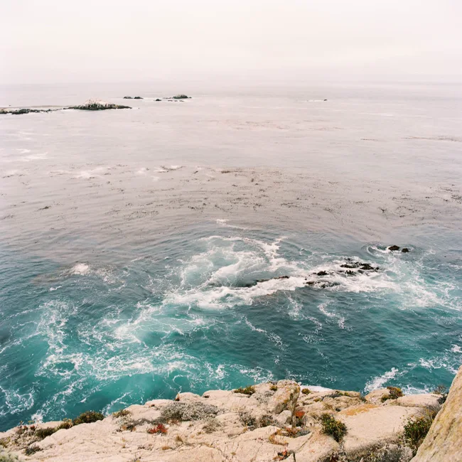 Turquoise waves swirling around rocks below a coastal overlook.