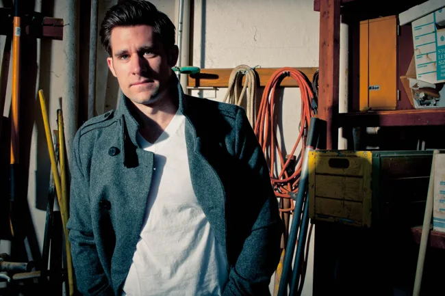 Man in a dark jacket and white T-shirt in a workshop.