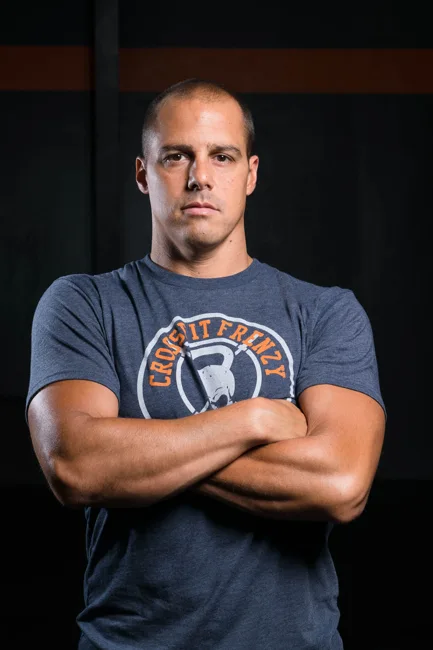 Man with folded arms seated against a dark background.