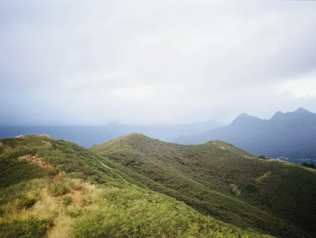 Rolling green ridgelines under a cloudy Hawaiian sky.