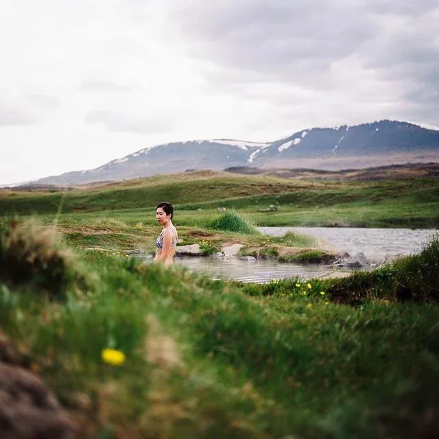 Person bathing in a small outdoor pool amid green hills.