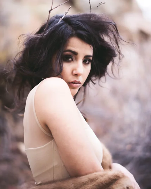 Close portrait of a dark-haired model with bare shoulders outdoors.