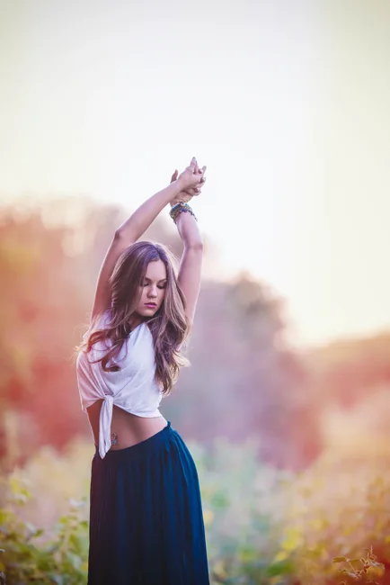 Woman raising her arms outdoors in warm, soft evening light.
