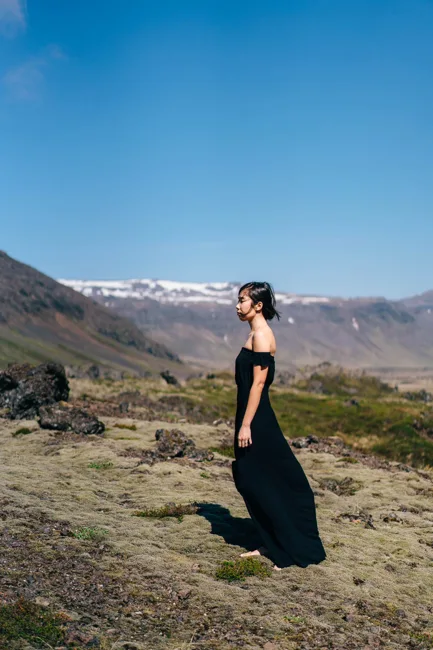 Model in a long black dress standing on a mountain slope.
