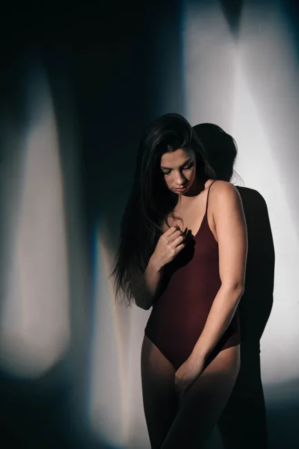 Model in a burgundy bodysuit looking down in a pool of light.