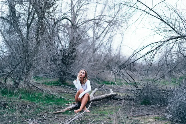 Wide view of a model sitting on a fallen tree in woodland.