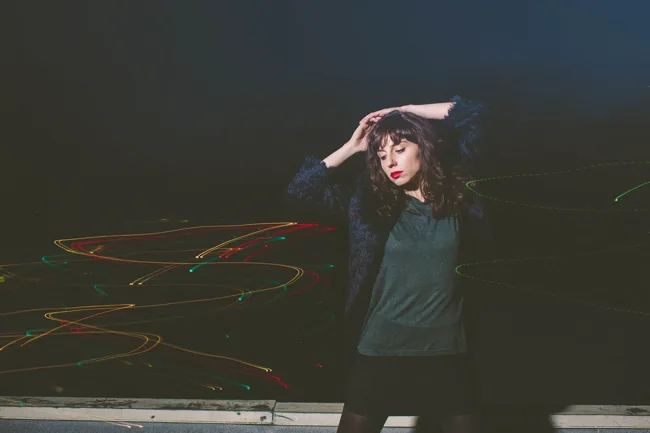 Model posing at night with colored light trails behind her.