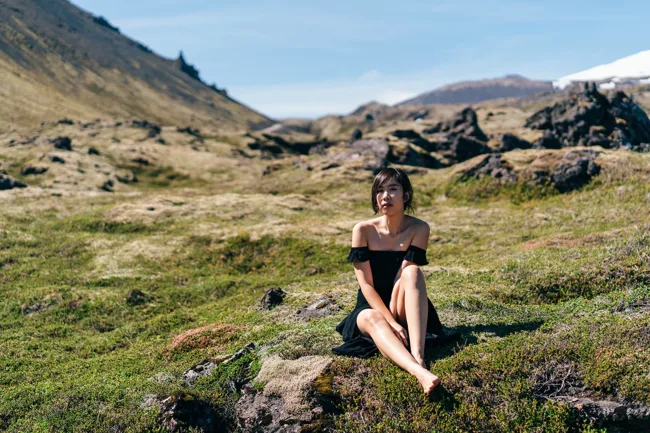 Model in a black dress sitting among rocks in a mountain landscape.