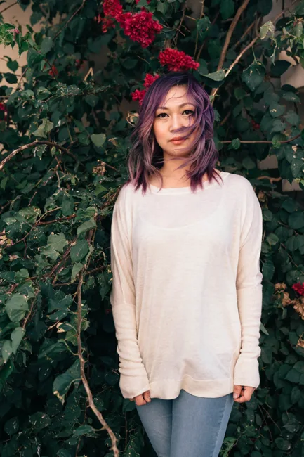 Woman in a white sweater and red hair accessory standing before ivy.