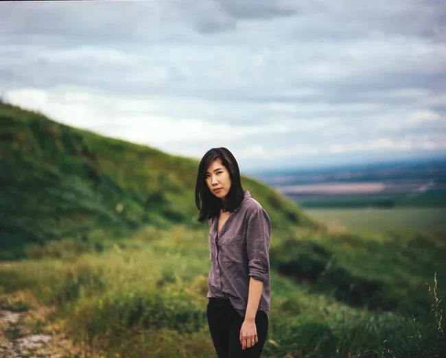 Woman standing on a green hillside beneath a cloudy sky.