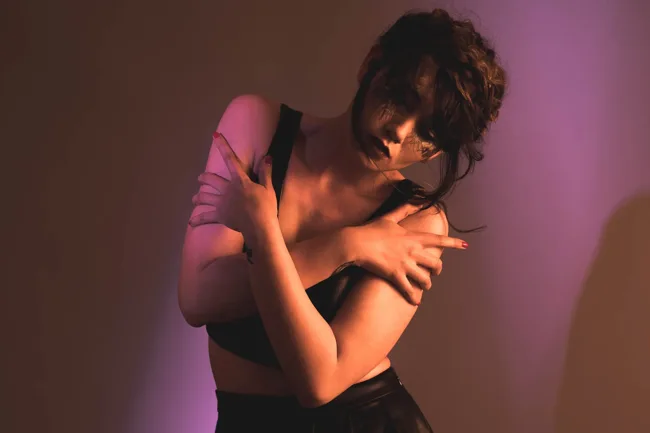 Model folding her arms across her shoulders in warm pink light.
