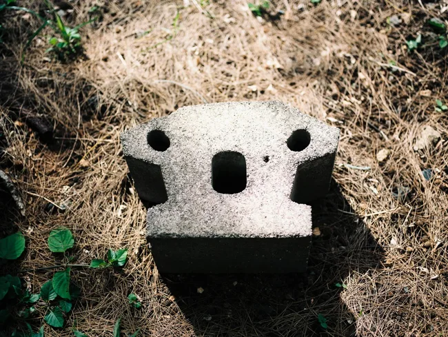 Weathered concrete block with three dark holes amid dry grass.