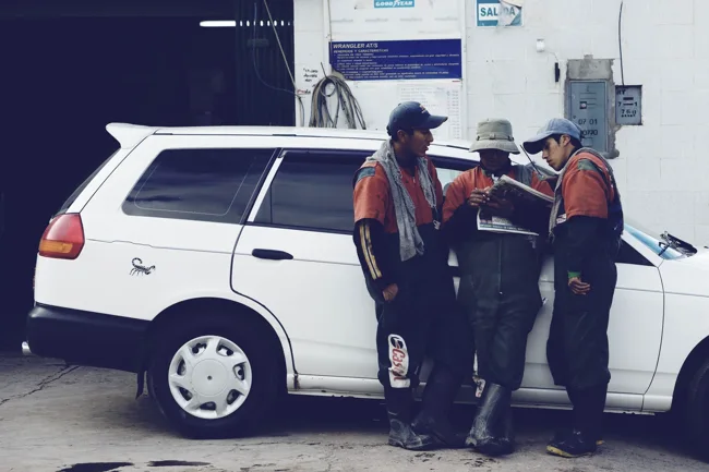 Several people standing beside a white vehicle on a street.