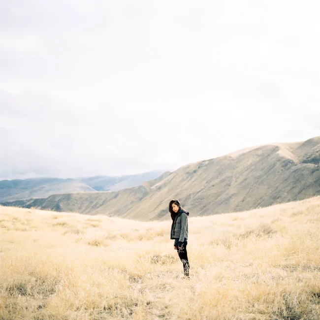 Distant figure standing in golden grass beneath mountain ridges.