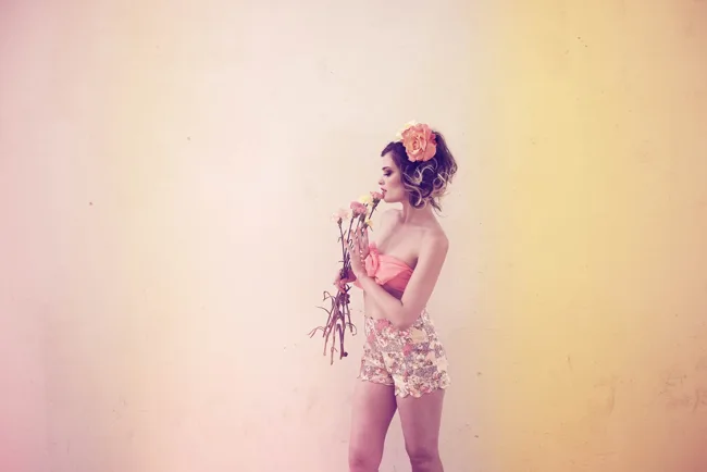 Model in a pink outfit posing against a warm pastel studio background.
