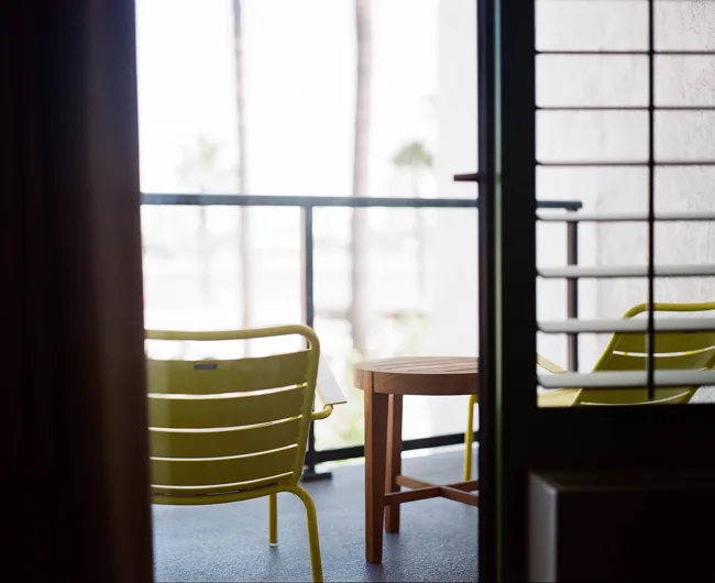 Green chairs and a small table on a bright balcony beyond a doorway.
