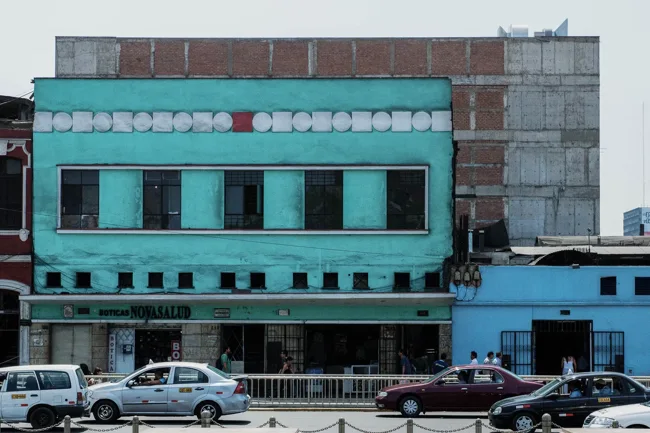 Turquoise building facade facing a street with parked cars.