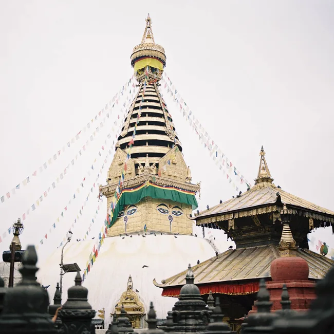 A stupa with painted eyes and a gold spire under an overcast sky.
