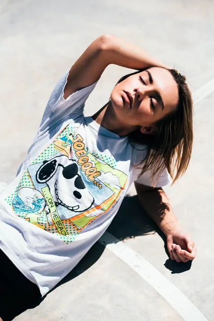 Model in a graphic shirt leaning back in bright sunlight.
