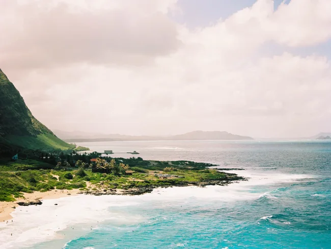 Turquoise surf along an Oahu beach below a green mountain slope.