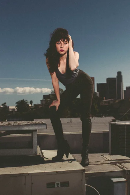 Model leaning forward on a rooftop above the city skyline.
