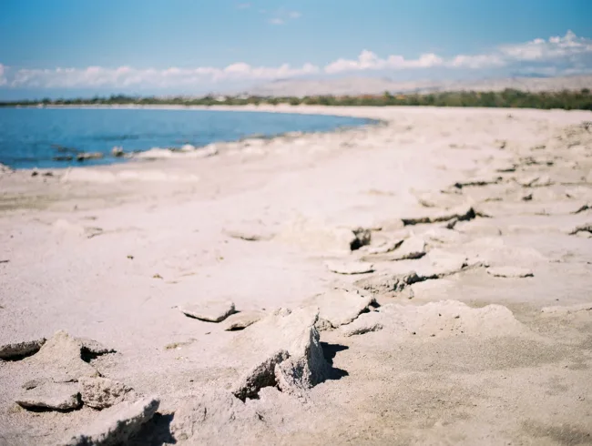 Pale, cracked shoreline beside the blue waters of the Salton Sea.