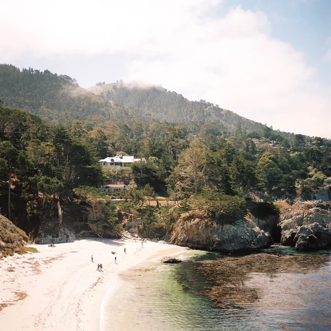 Small sandy cove below wooded coastal hills.