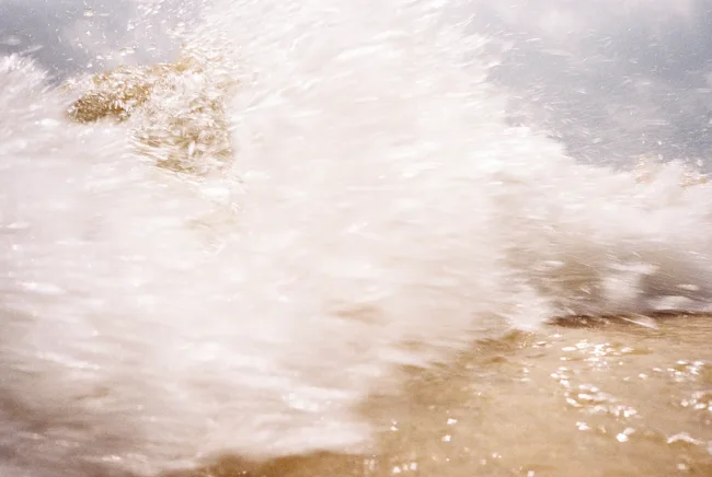 Soft white foam washing across sunlit beach sand.