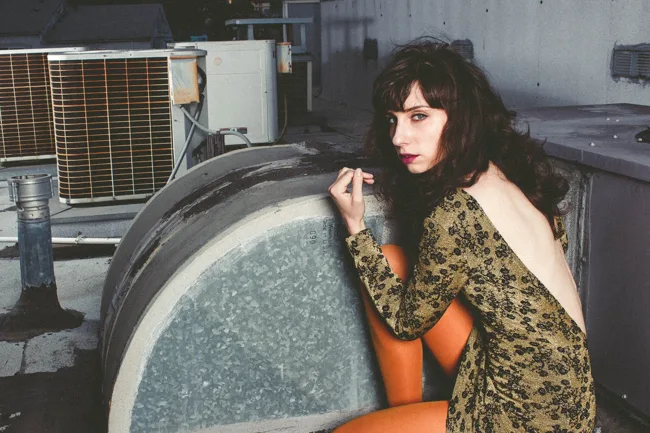 Model wearing a patterned dress and orange tights beside rooftop machinery.