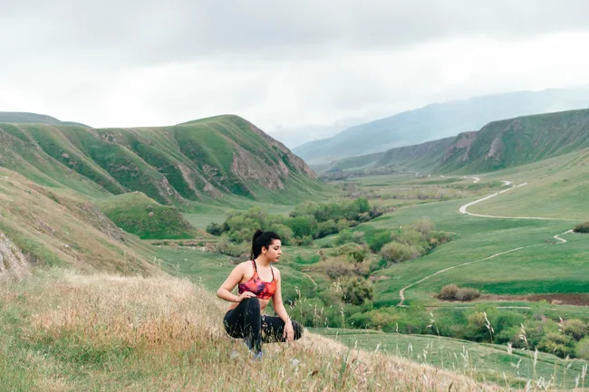 Hiker seated on a grassy slope above a broad green valley.