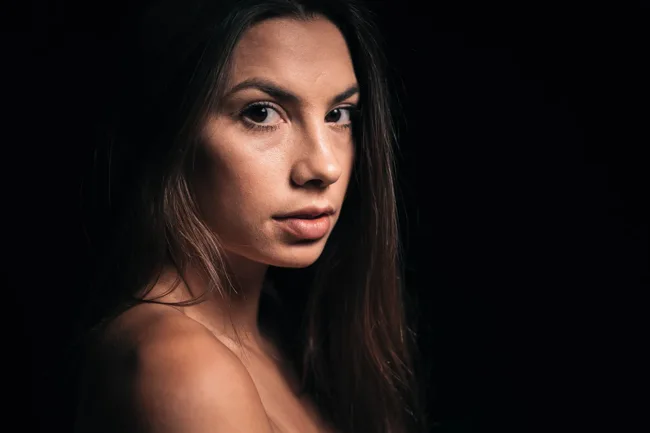 Close portrait of a dark-haired woman against a black background.