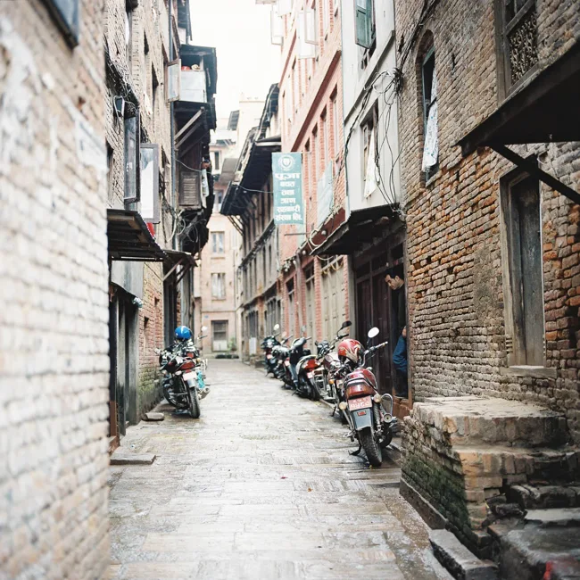 Narrow lane between tall brick buildings with parked motorcycles.